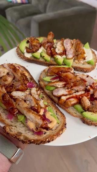 A plate of avocado toast with chicken is being held up in a living room
